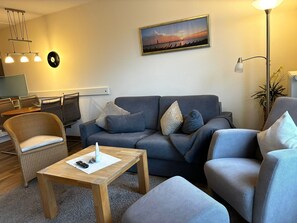 Een moderne woonkamer met een grijze bank, een houten salontafel en een eethoek met stoelen en een tafel.
