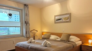 A neatly made bed with two towels, a wooden headboard, a bedside table with a lamp, and a framed picture on the wall. - TRA-152 - Residence Trafalgar (Cuxhaven)