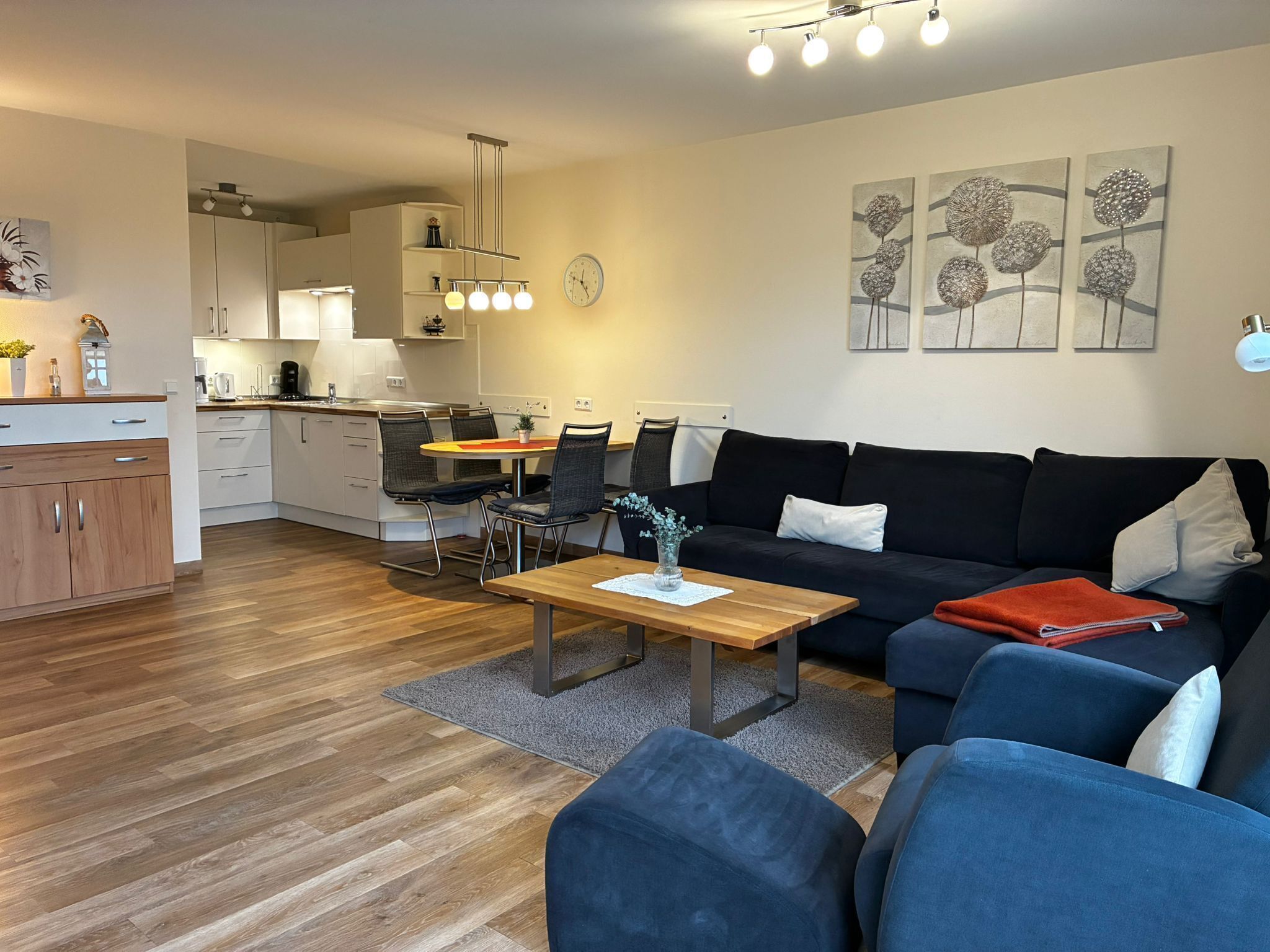 Ein modernes Wohnzimmer mit einer schwarzen Couch, einem Holztisch und einem Essbereich mit rundem Tisch und Stühlen.