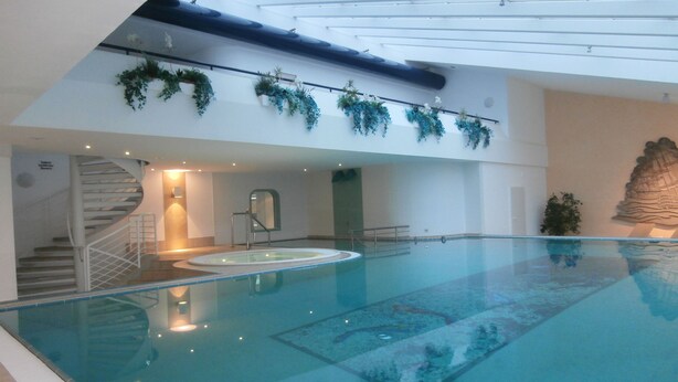 An indoor swimming pool with a glass ceiling, stairs, and decorative plants. - TRA-230 - Residence Trafalgar (Cuxhaven)