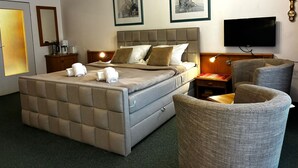A hotel room with a large bed, two framed artworks on the wall, a flat-screen TV, and a seating area with a chair and a small table. - TRA-230 - Residence Trafalgar (Cuxhaven)