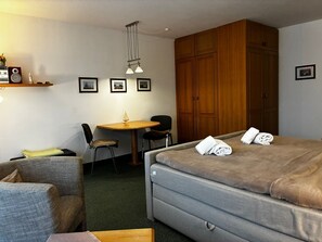 Une chambre d’hôtel comprenant un lit, un bureau avec des chaises, une armoire et des tableaux encadrés accrochés au mur.