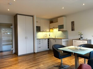 A modern kitchen with white cabinets, a dining table with chairs, and a wooden floor. - TRA-347 - Residence Trafalgar (Cuxhaven)