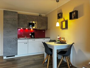 Une cuisine moderne avec des meubles gris, un pare-feu rouge et une table à manger blanche accompagnée de deux chaises.