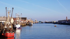 A harbor with boats docked along the piers, a clear sky, and a distant clock tower. - TRA-525 - Residence Trafalgar (Cuxhaven)