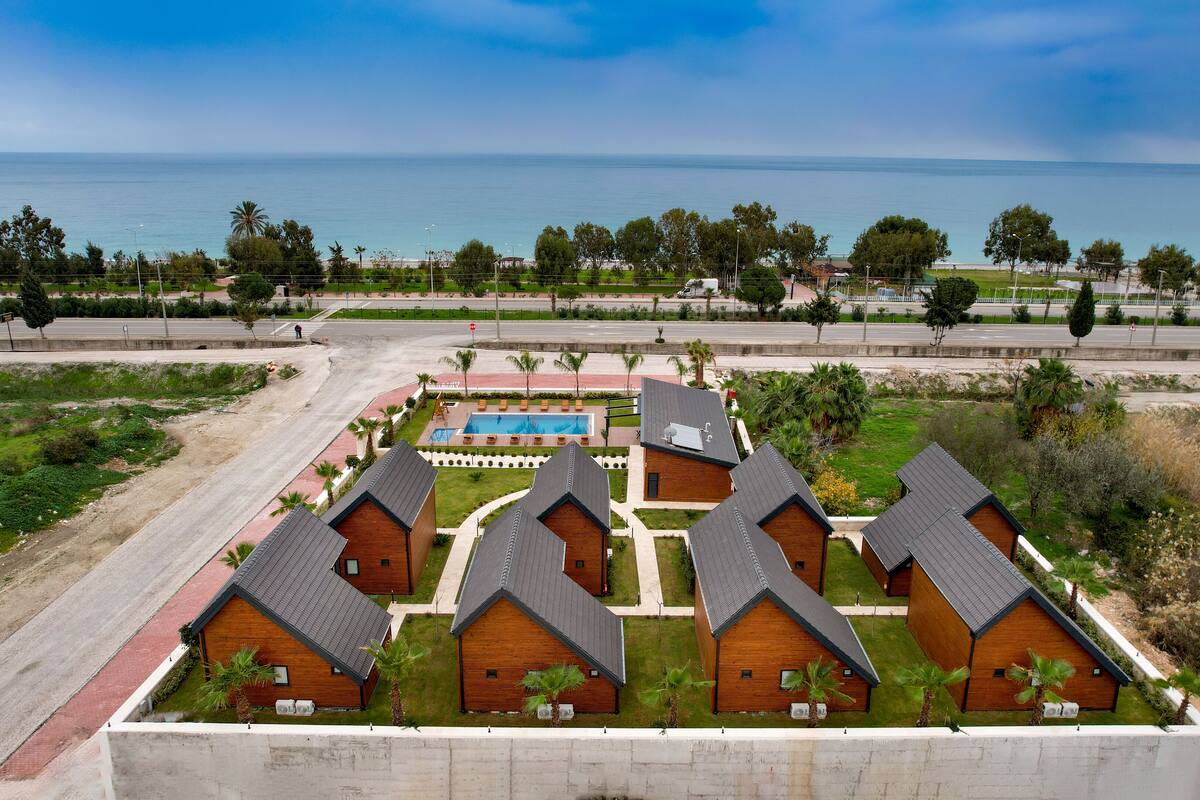 A resort with multiple wooden cabins, a swimming pool, and a view of the ocean.
