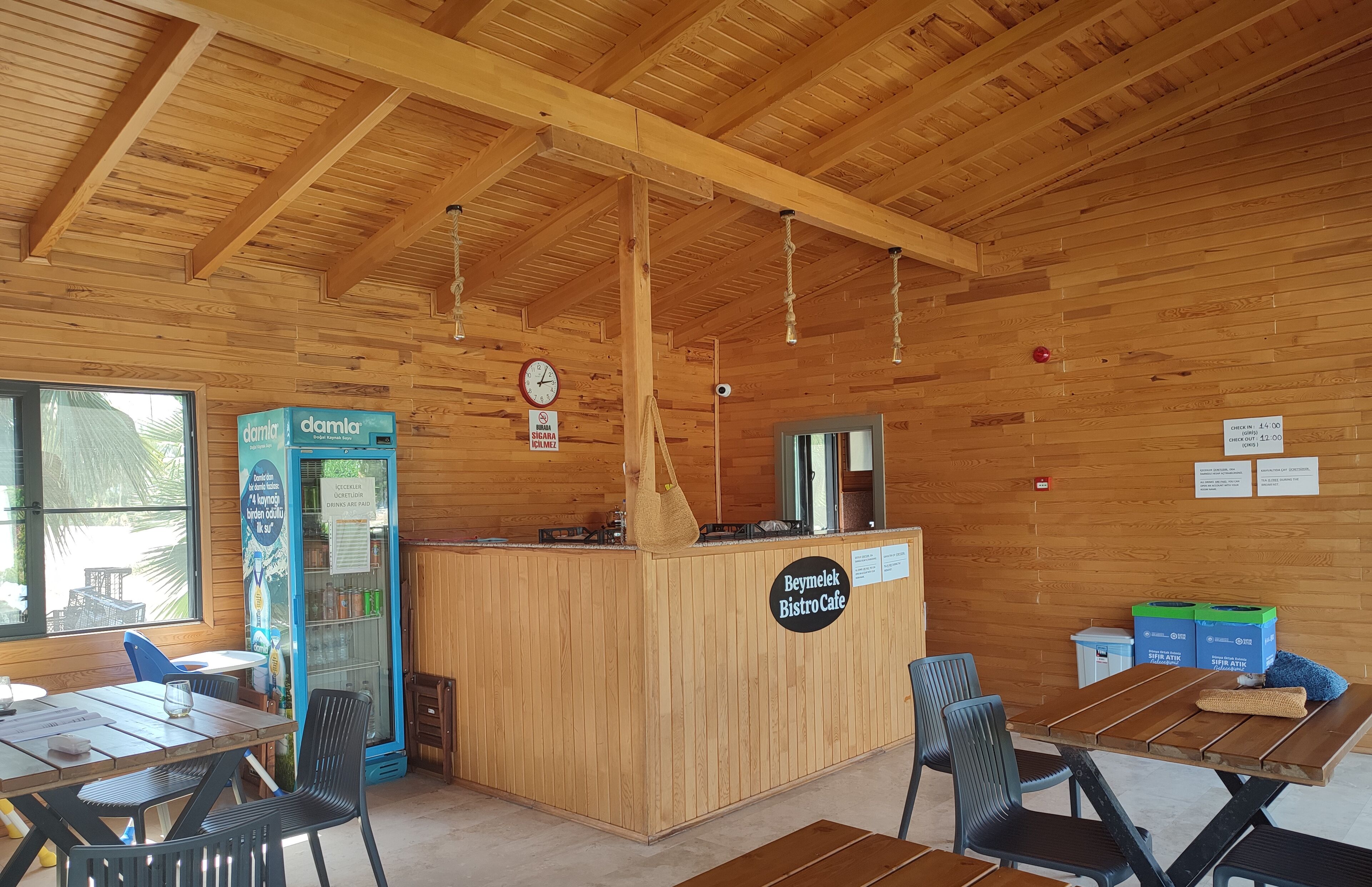 A wooden interior with a counter labeled "Beymekel Bistro Cafe," a refrigerator, and seating arrangements.