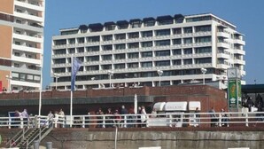Un hôtel à plusieurs étages, doté de balcons, d’une base en briques et surplombant un ciel dégagé.