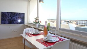 Un coin repas avec une table dressée pour deux personnes, un téléviseur fixé au mur et une fenêtre donnant sur la ville.