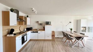 Una cuina moderna amb armaris blancs, un taulell de fusta i una zona de menjador amb taula i cadires.