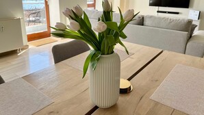 Un saló amb taula de dinar de fusta, un vas de flors blanc, un sofà gris i un televisor fixat a la paret.