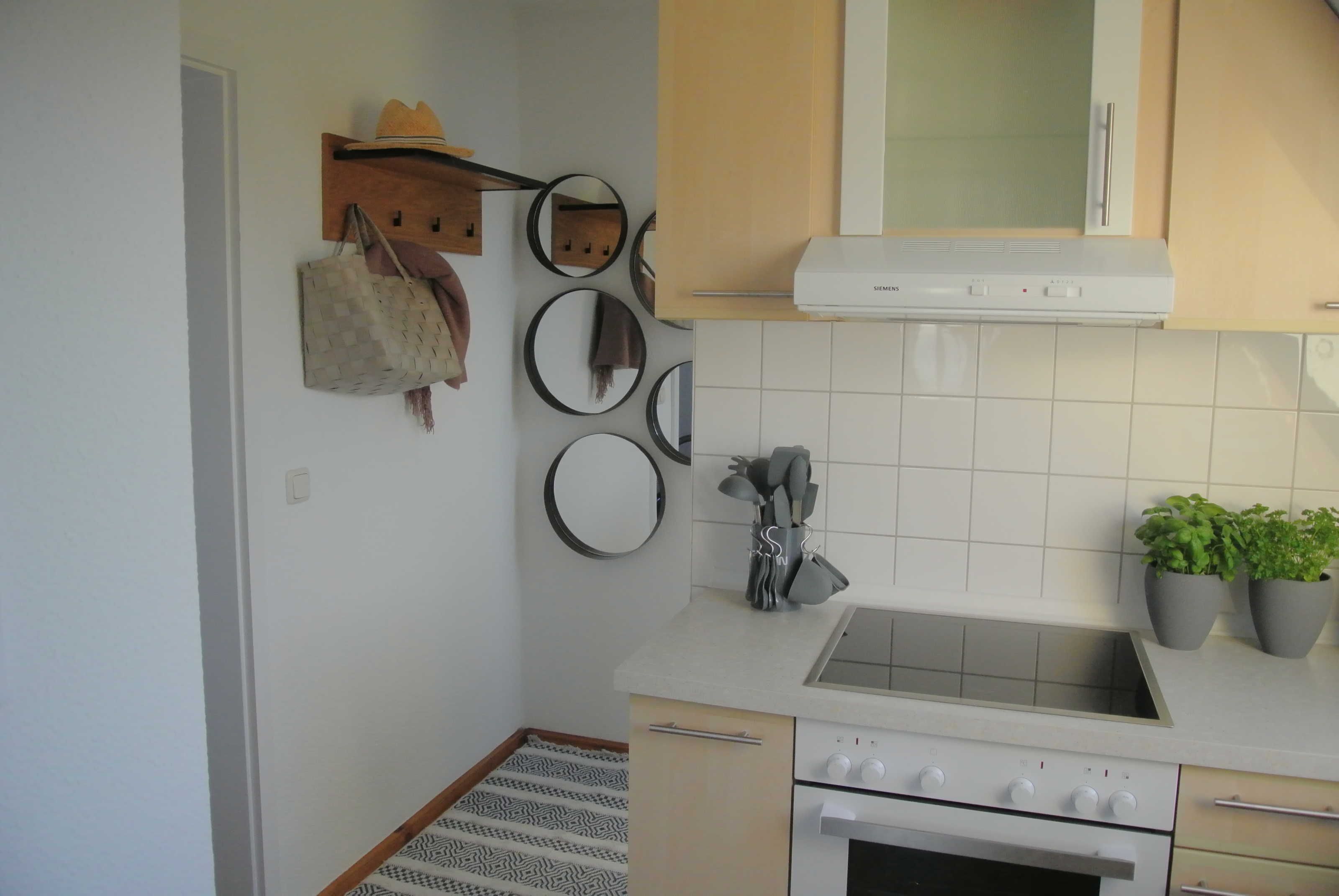 A kitchen with a white stove, a sink, and cabinets. There are potted plants on the counter and a hanging hat and bag on the wall.