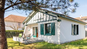 Ein kleines, eingeschossiges Haus mit geneigtem Dach, grünen Fensterläden und einer Veranda mit einer Bank.