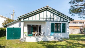Ein kleines, eingeschossiges Haus mit grüner Tür und Fenstern, einer Veranda mit Tisch und Stühlen sowie einem grünen Rasen.