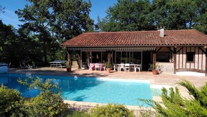 Ein Poolbereich mit überdachter Terrasse, Sitzgelegenheiten im Freien und Blick auf den Pool.