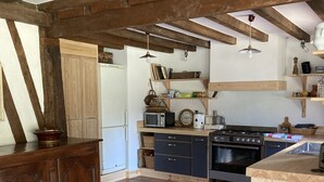 Eine rustikale Küche mit sichtbaren Holzbalken, einer Holzauslage und einem Fliesenboden.