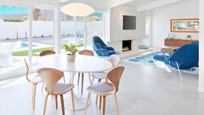 A modern living room with a dining area, a fireplace, and a pool view.