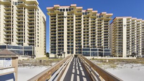 Ein Strandhotel mit mehreren Hochhäusern, einer Holzpromenade, die zum Strand führt, und einem klaren, blauen Himmel.
