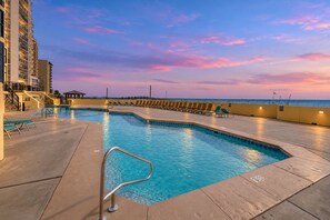 A swimming pool with a curved edge, surrounded by lounge chairs and a building with multiple floors. - Phoenix II 2066 | Pools, Hot Tubs, Tennis & more | Oceanfront | My Beach Getaways (Orange Beach)