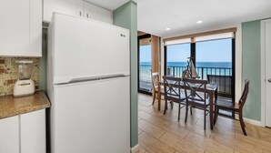 Eine moderne Küche mit einem weißen Kühlschrank, einem Mixer auf der Arbeitsfläche und einem Essbereich mit Tisch und Stühlen.