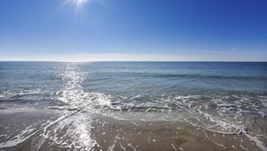 Ein Strand mit blauem Himmel und Sonnenlicht, das sich im Wasser spiegelt.
