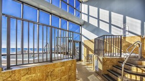 Ein modernes Interieur mit großen Fenstern mit Blick auf einen Strand, einer Treppe und einem Meerblick.