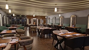 Restaurante com mesas e cadeiras de madeira, piso com padrão herringbone e luminárias pendentes.