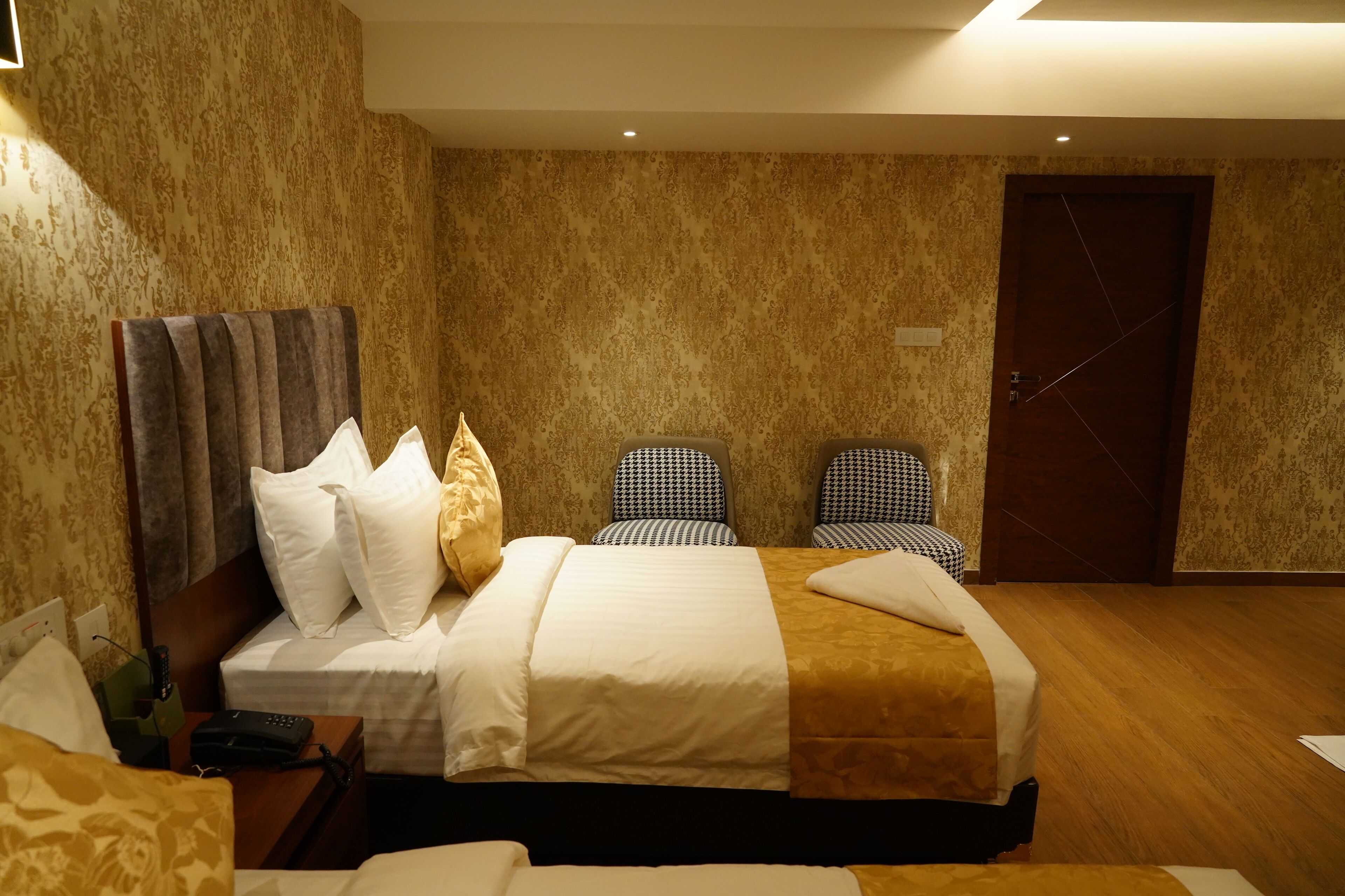 Een hotelkamer met een groot bed, twee stoelen, een houten vloer en een deur.