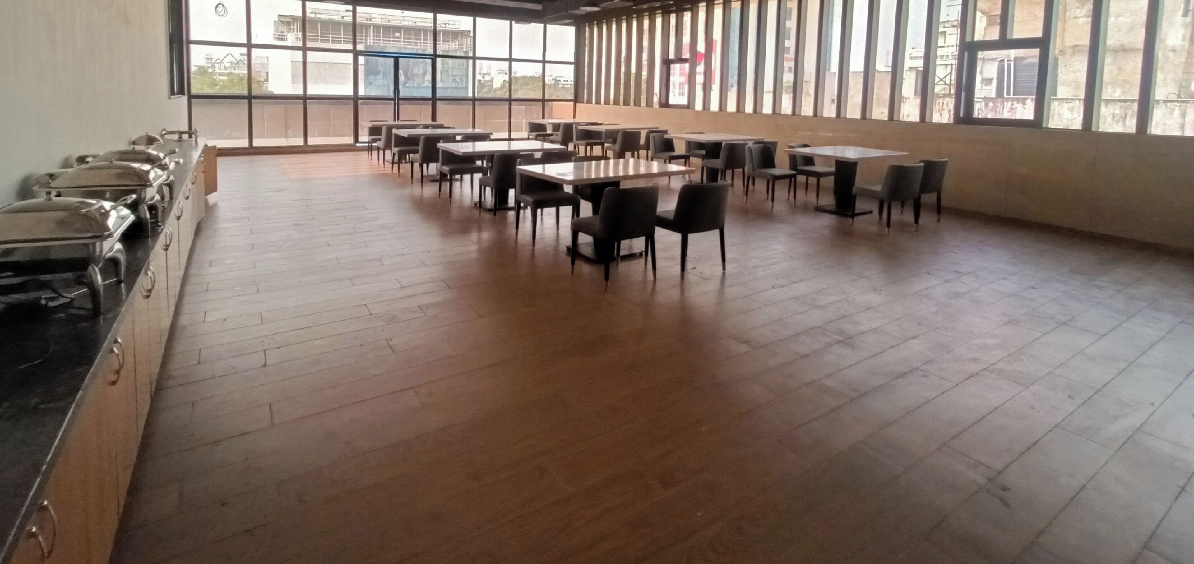 Une pièce spacieuse avec de nombreuses tables et chaises, de grandes fenêtres et un espace buffet.