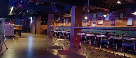 Un bar intérieur avec un plancher en bois, des tabourets de bar en métal et des murs en briques.