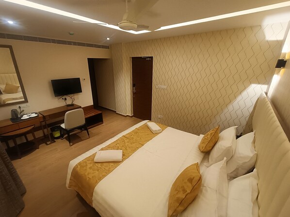 A hotel room with a bed, a desk, a chair, a television, and a door.