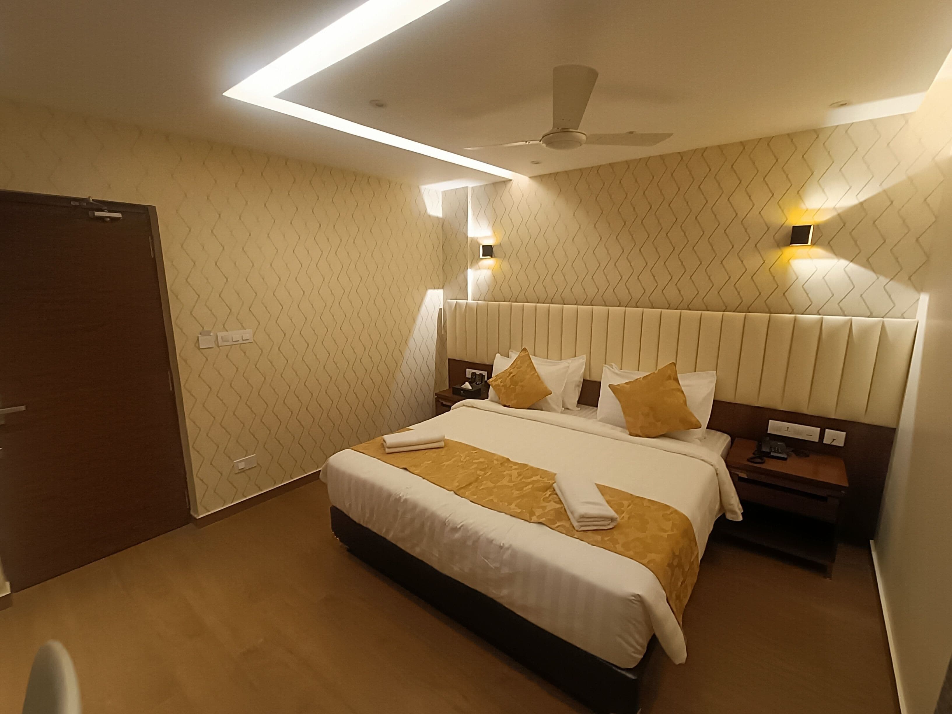 Hotellihuone, jossa on suuri sänky, kattotuuletin ja kaksi yöpöytää.