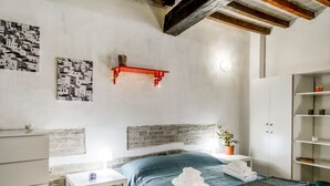A bedroom with a bed, a white dresser, a nightstand, a red shelf, a wall-mounted light, and a potted plant. - Studio located on the ground floor of a building from 1900.In 35 square meters of space it accommodates up two people with a double sofa bed.In a quiet and residential location, right in the center.We are located within the ZTL (limited traffic area).Con (Parma)