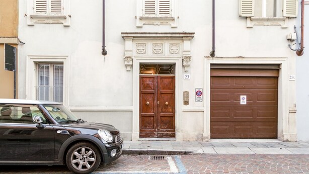 A black car parked in front of a building with a double door and a garage door, a cobblestone street, and a number '23' sign. - Studio located on the ground floor of a building from 1900.In 35 square meters of space it accommodates up two people with a double sofa bed.In a quiet and residential location, right in the center.We are located within the ZTL (limited traffic area).Con (Parma)