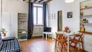 A room with a bed, a desk, a chair, a radiator, a window with curtains, a shelf with bottles, and a hanging light. - Studio located on the ground floor of a building from 1900.In 35 square meters of space it accommodates up two people with a double sofa bed.In a quiet and residential location, right in the center.We are located within the ZTL (limited traffic area).Con (Parma)