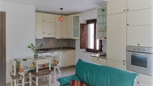 Una cocina compacta con armarios blancos, una mesa de comedor con sillas y un sofá color turquesa con cojines.