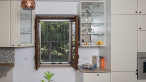 Una cocina con ventanal, una mesa con mantel floral y una repisa con utensilios de cocina.