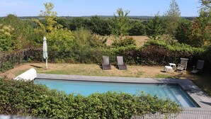 A swimming pool with lounge chairs and a table, surrounded by greenery and trees. - Green cottage (Sainte-Marguerite-de-Carrouges)