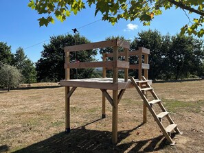 Une structure en bois avec une échelle, située dans un champ herbeux, avec des arbres en arrière-plan.