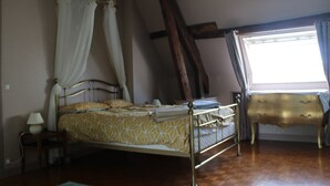 A bedroom with a four-poster bed, a bedside table with a lamp, a wooden dresser, and a window with curtains. - Green cottage (Sainte-Marguerite-de-Carrouges)