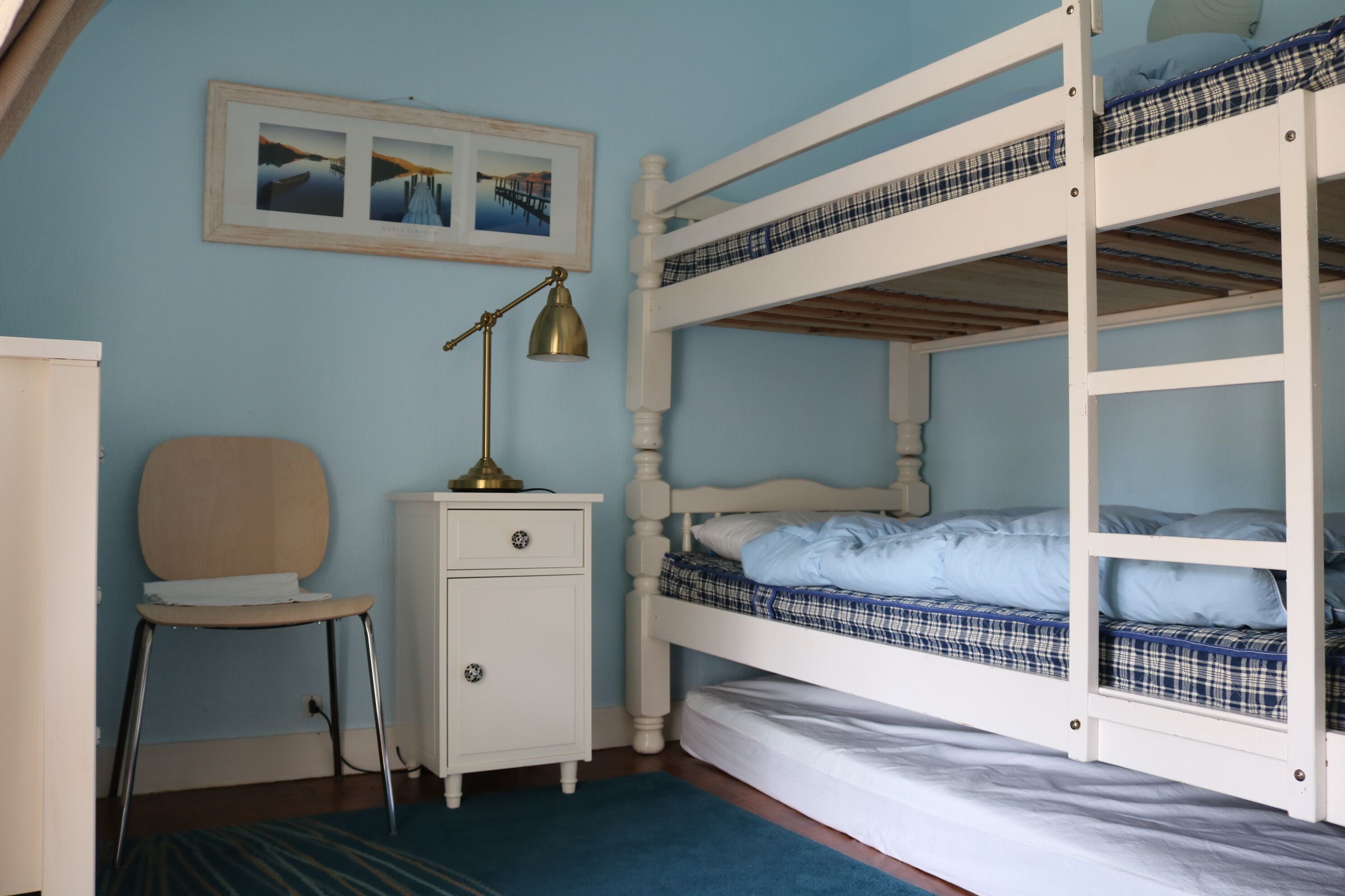 A bunk bed room with a desk and chair, a lamp, and a framed picture on the wall.