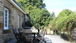 A stone building with a patio table and chairs, surrounded by greenery. - Green cottage (Sainte-Marguerite-de-Carrouges)