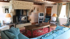 A cozy living room with a stone fireplace, a sofa, a coffee table, and a television. - Green cottage (Sainte-Marguerite-de-Carrouges)