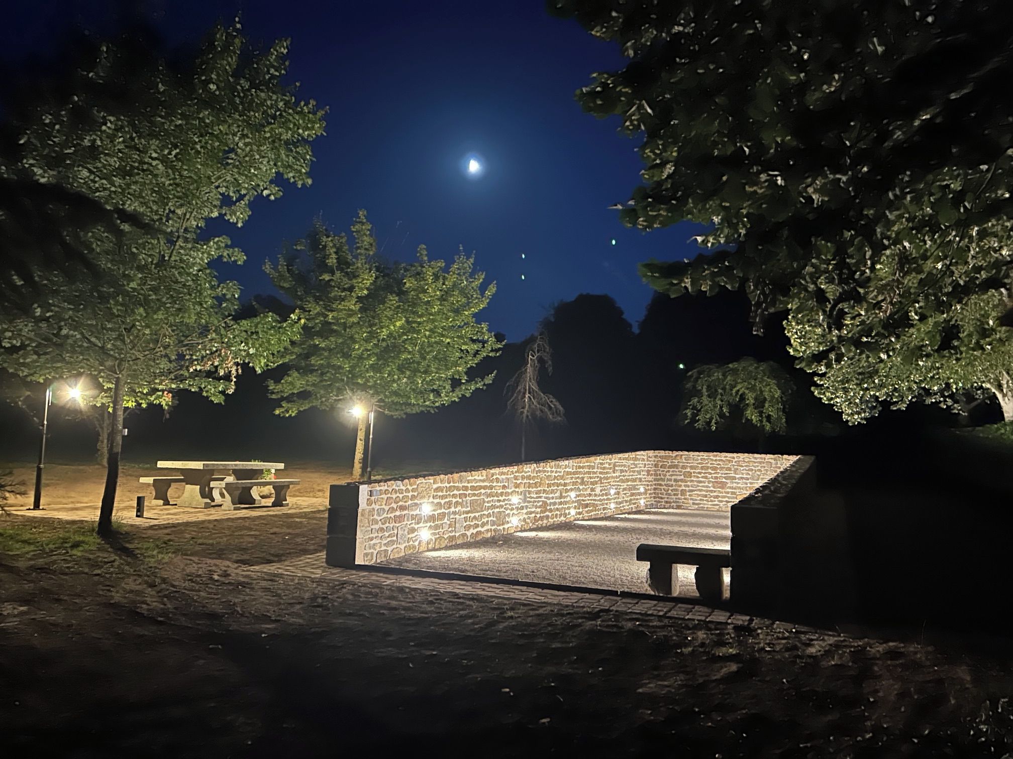 Un espace extérieur aménagé pour la nuit, avec un mur en pierre, un banc et une table de pique-nique.