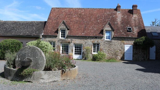 A stone building with a red-tiled roof, multiple windows, and a gravel driveway. - Green cottage (Sainte-Marguerite-de-Carrouges)