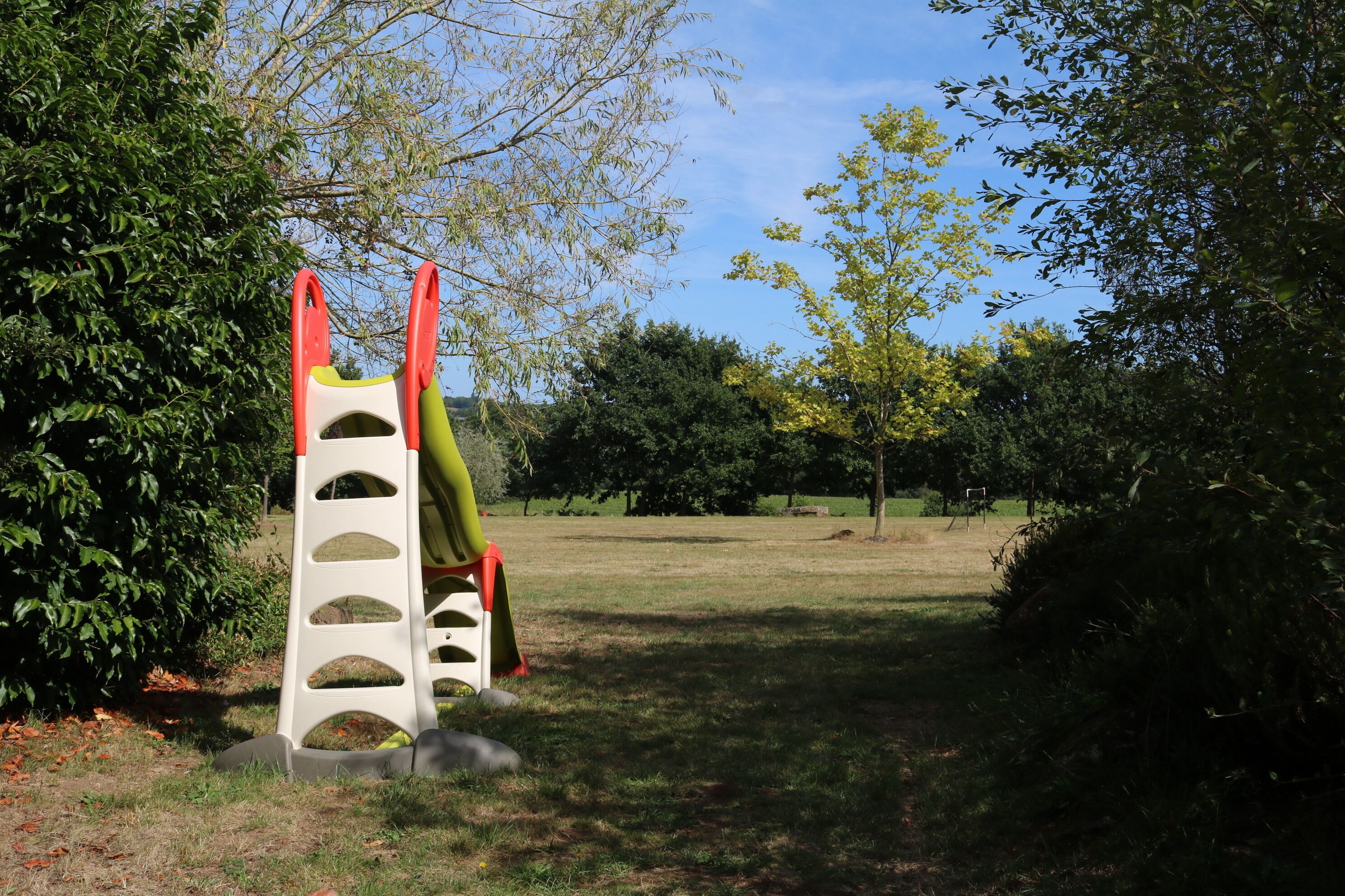 Un parque infantil con una estructura de escalada y un tobogán, rodeado de árboles y césped.