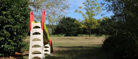 Un parque infantil con una estructura de escalada y un tobogán, rodeado de árboles y césped.