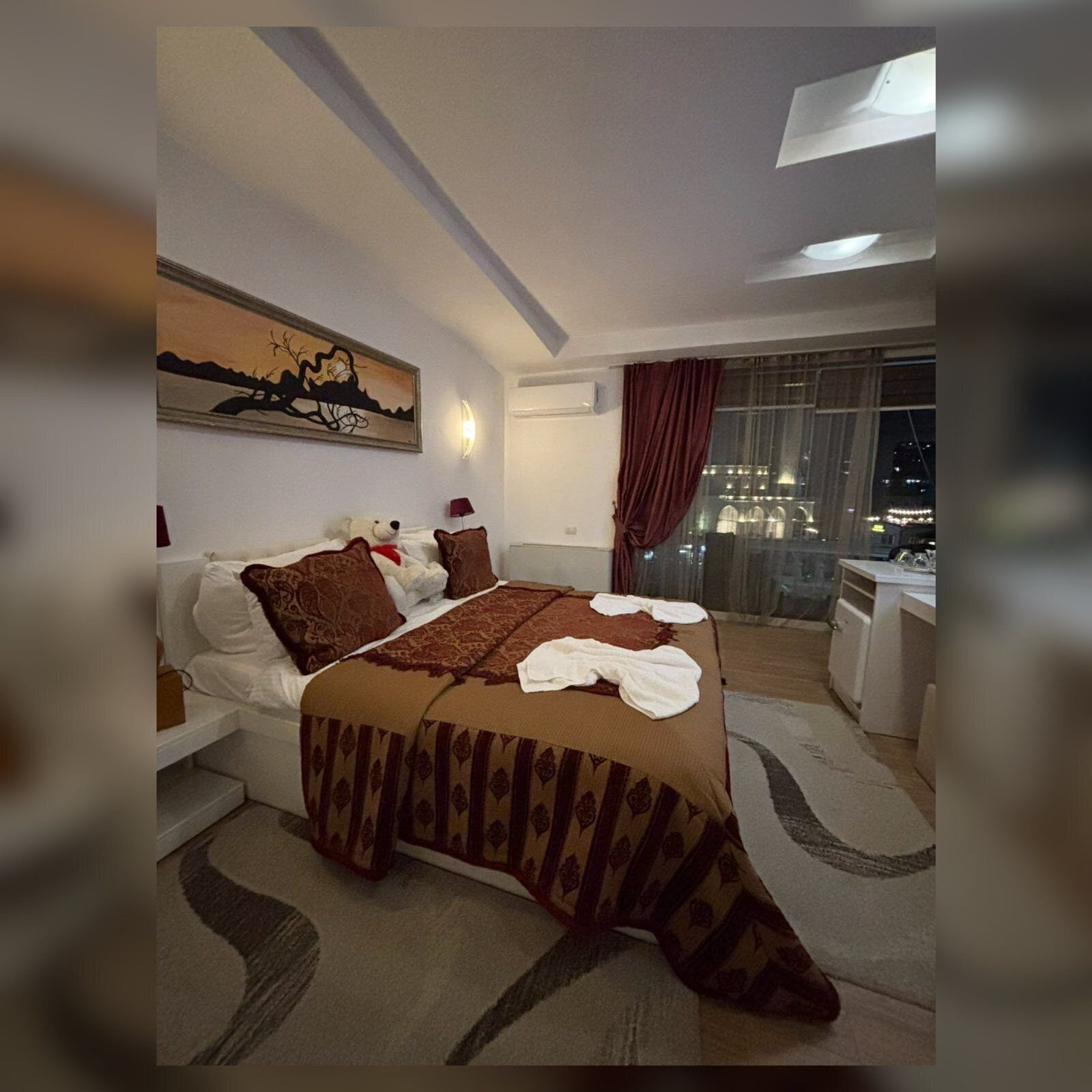 Camera da letto moderna con un letto grande, un quadro al muro e vista sulla città di notte.