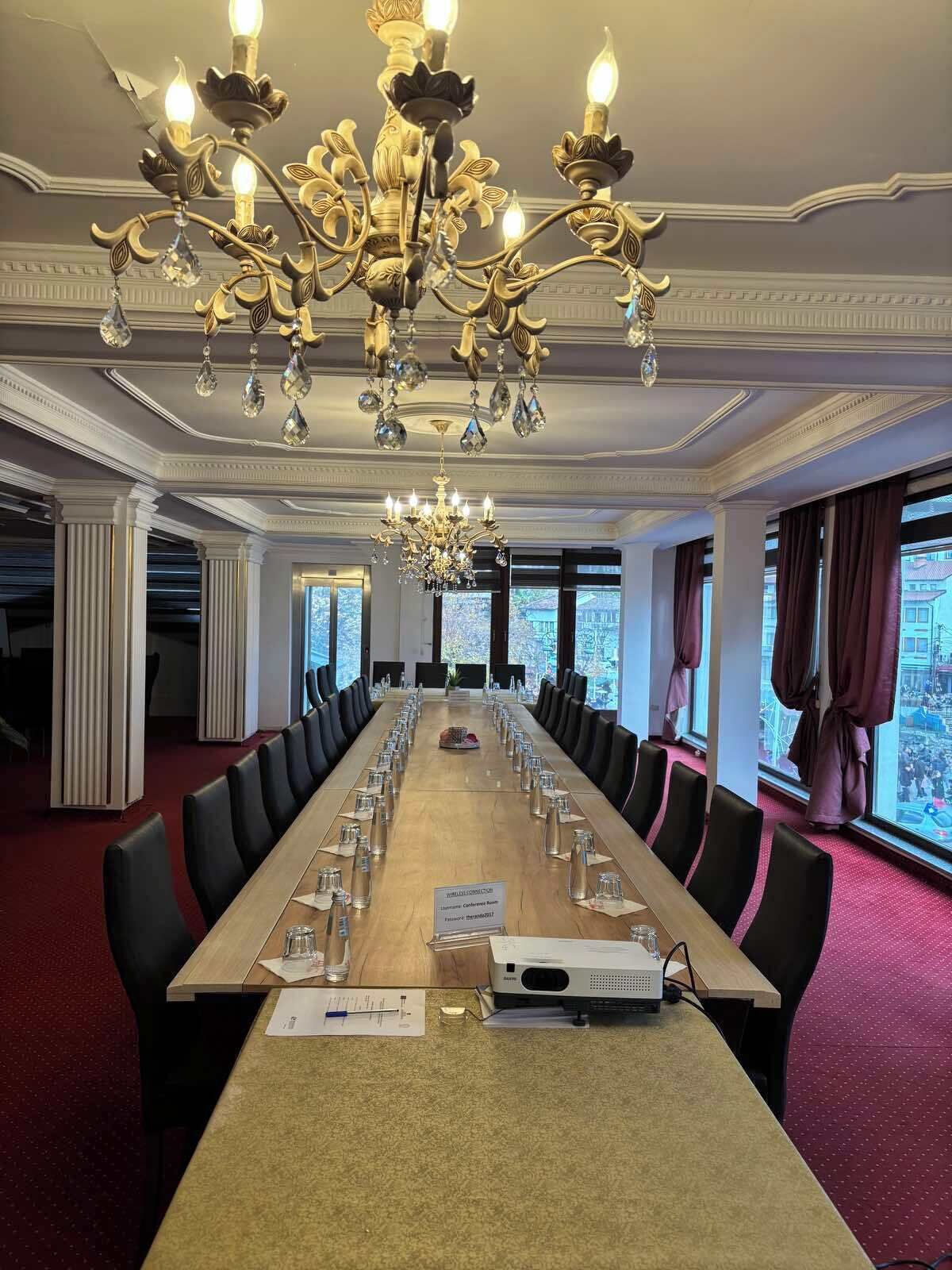 A conference room with a long table, chairs, a chandelier, and large windows.