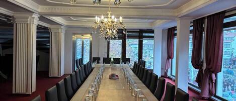 A conference room with a long table, chairs, a chandelier, and large windows.